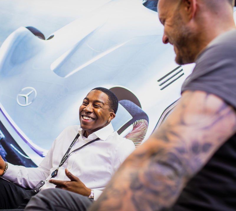Two men laughing in front of an Mercedes-Benz car poster